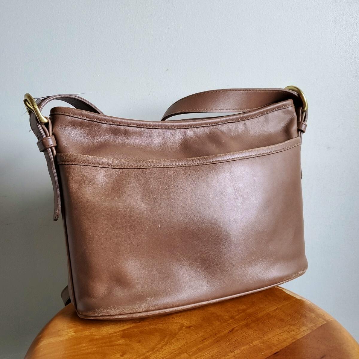 Brown leather Old Coach shoulder bag shown on a wooden surface against a light wall.