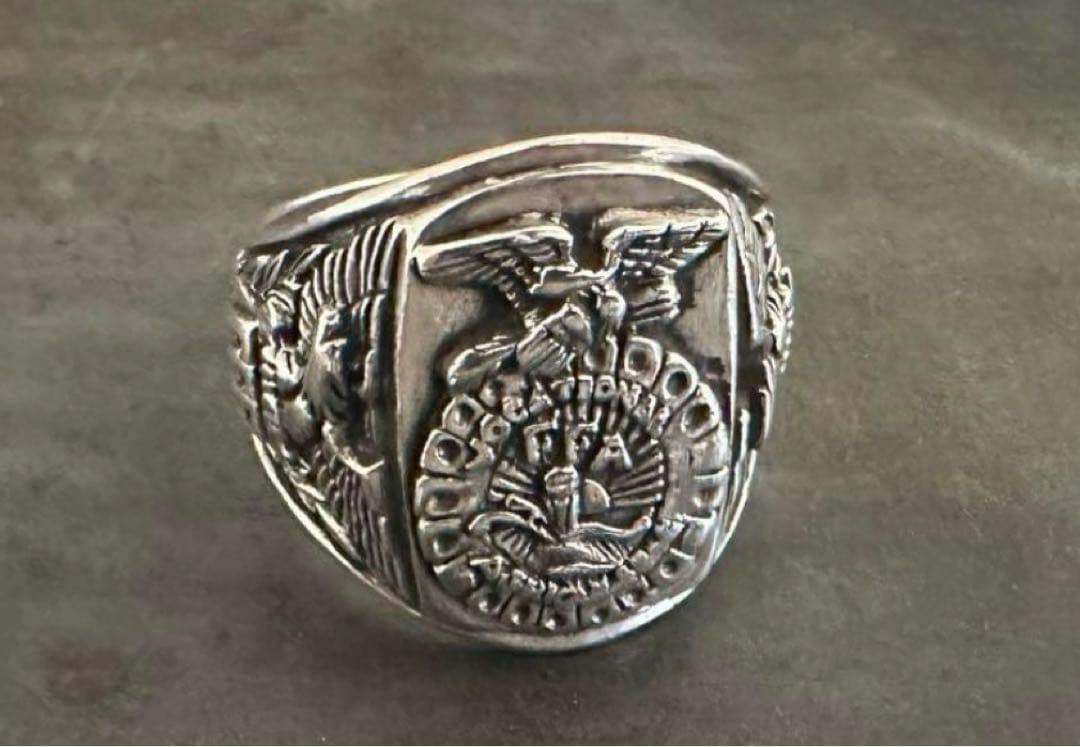 Close-up photo of a vintage army silver ring showing its engraved emblem and side detailing on a dark surface.