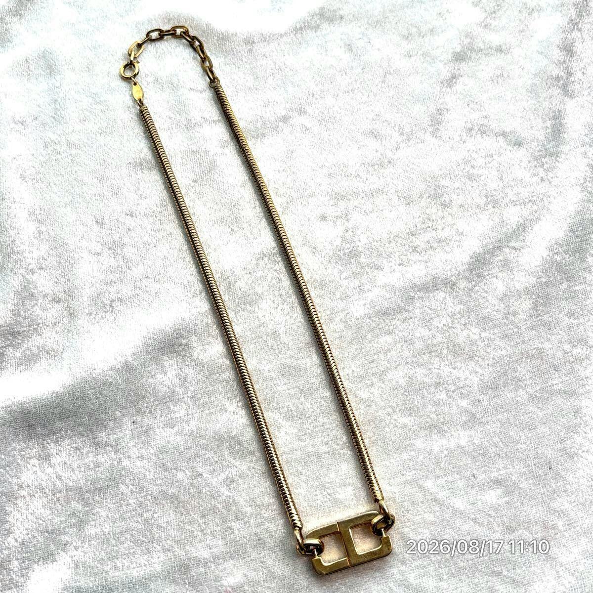Gold-colored Christian Dior wire/omega chain necklace with a CD-style rectangular logo link laid flat on white fabric.