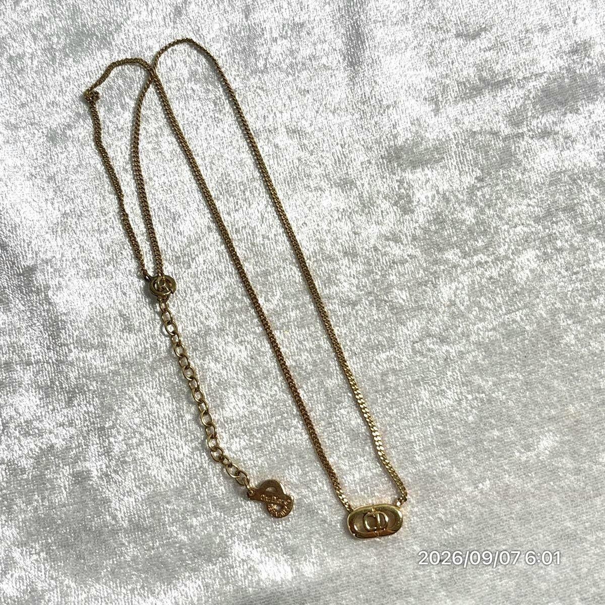 Gold-colored Christian Dior necklace with a double CD logo pendant and chain laid on a light fabric background.