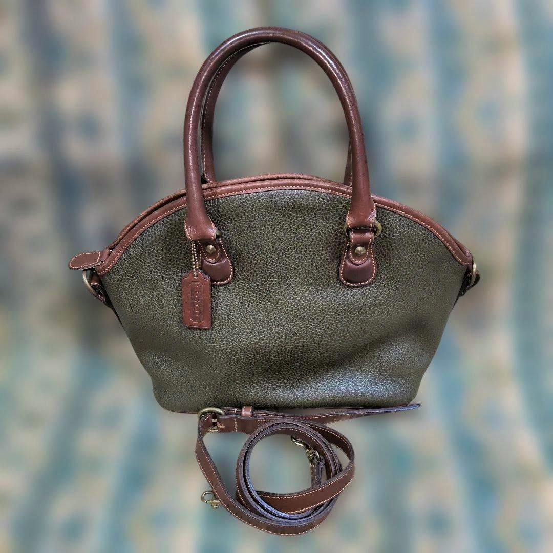 A green pebbled leather Old Coach 2-way shoulder bag with brown leather handles and a coiled detachable shoulder strap visible.