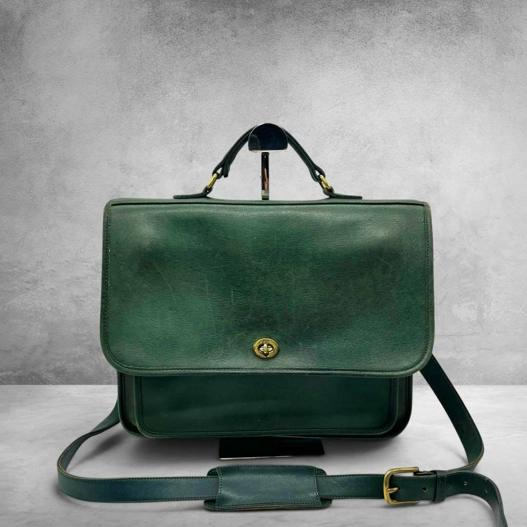 Green leather Coach briefcase shown front-facing with a top handle, front turn-lock closure, and an adjustable shoulder strap.