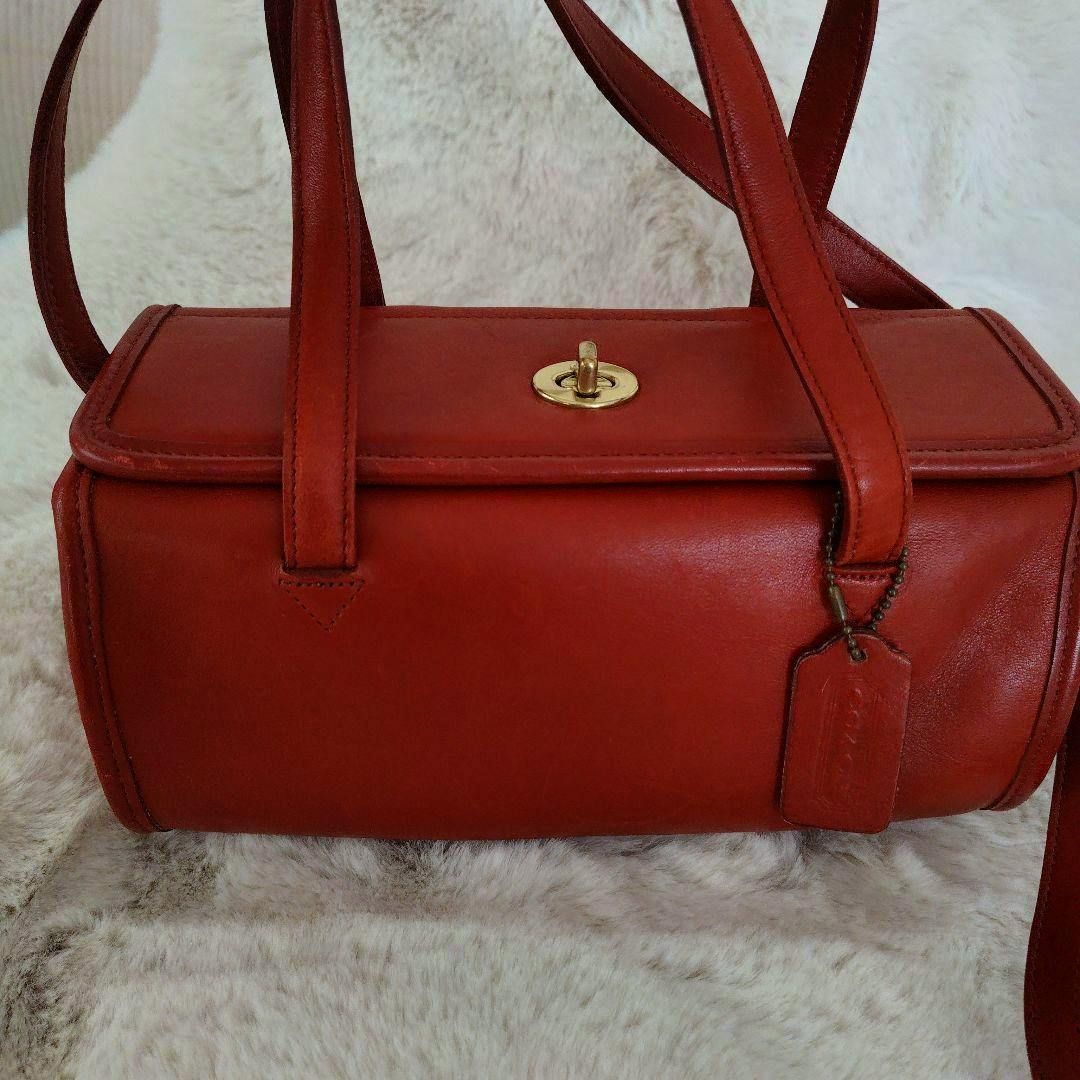 Red leather shoulder bag shown from the front with a top turn-lock closure and a hanging leather tag on a light fur background.