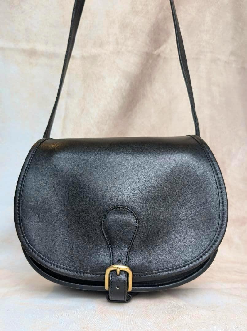 Front view of a black Coach saddle bag showing the curved flap, front buckle, and shoulder strap.
