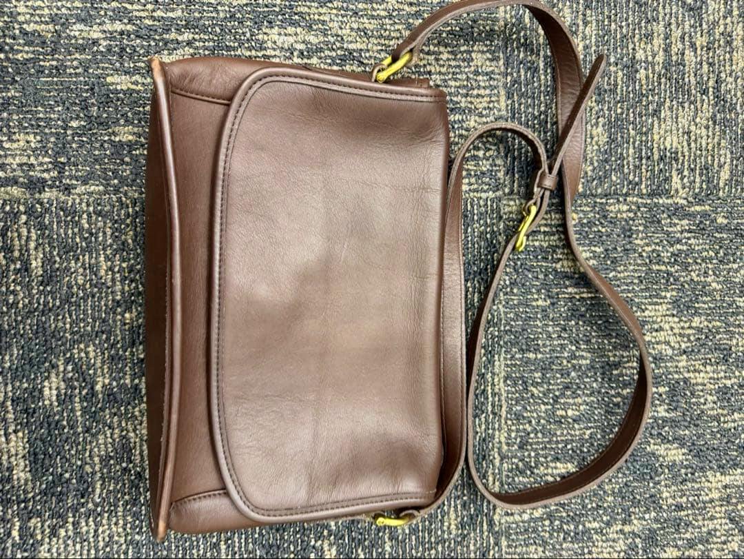 Brown Coach Curtis leather shoulder bag with strap laid flat on a carpeted surface.