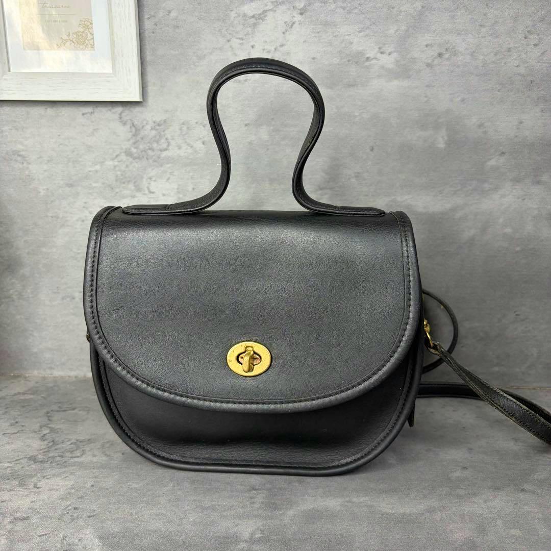 Front view of a black vintage COACH 2way Bella Court leather bag with a gold turn-lock closure and top handle.