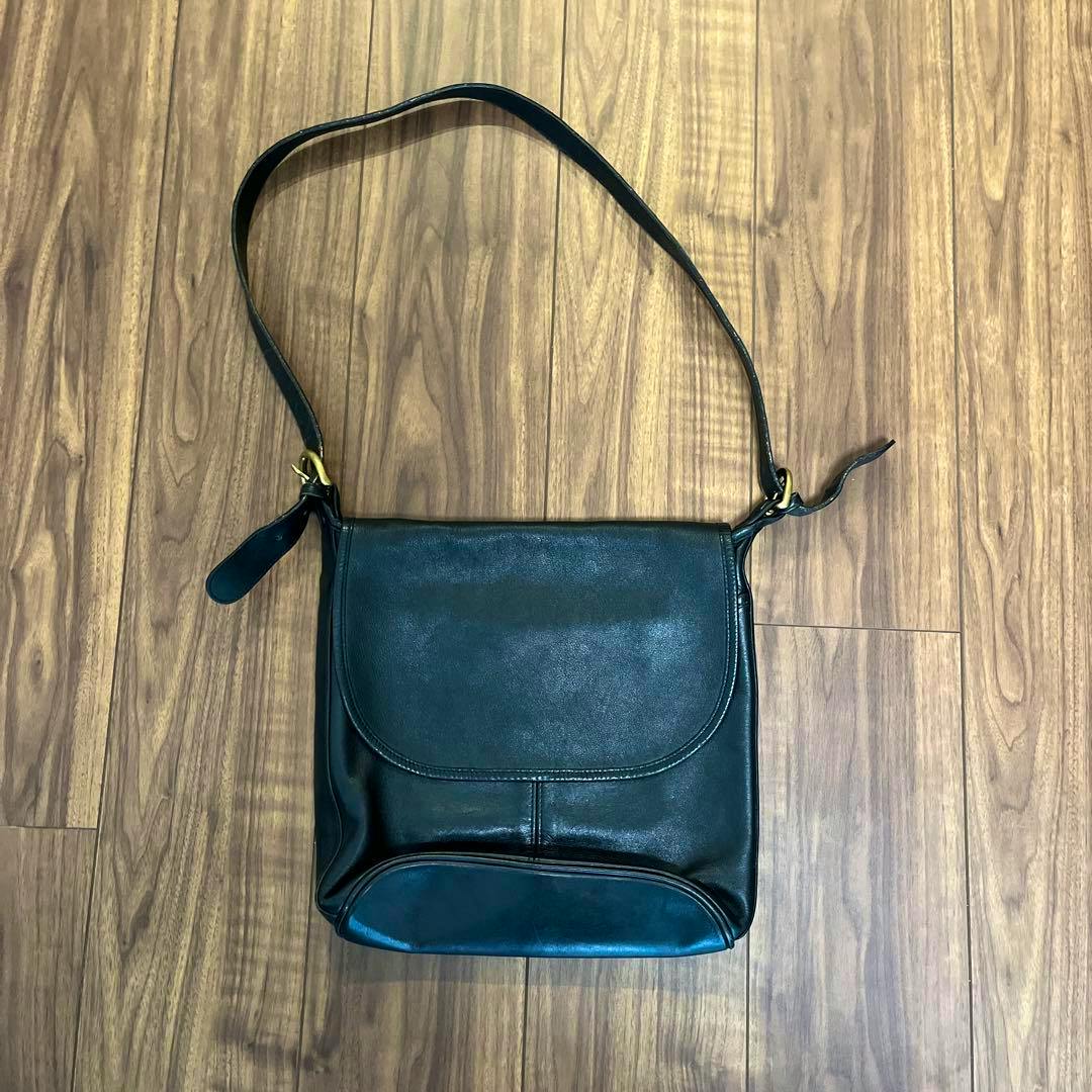 Black vintage Coach cow leather shoulder bag laid flat on a wood floor with the flap closed.