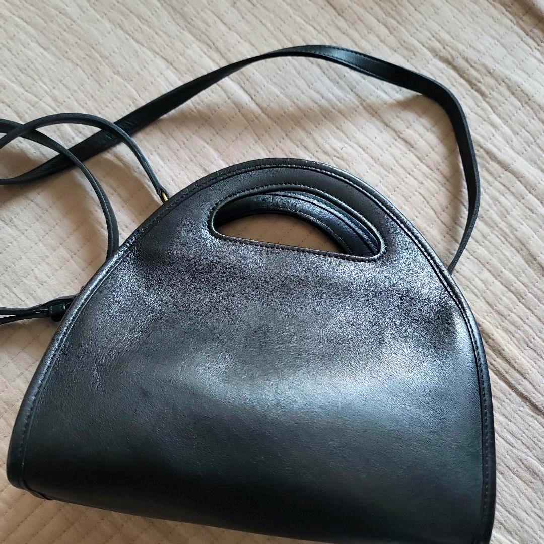 Black Old Coach cow leather shoulder bag with a built-in handle and long shoulder strap on a quilted background.