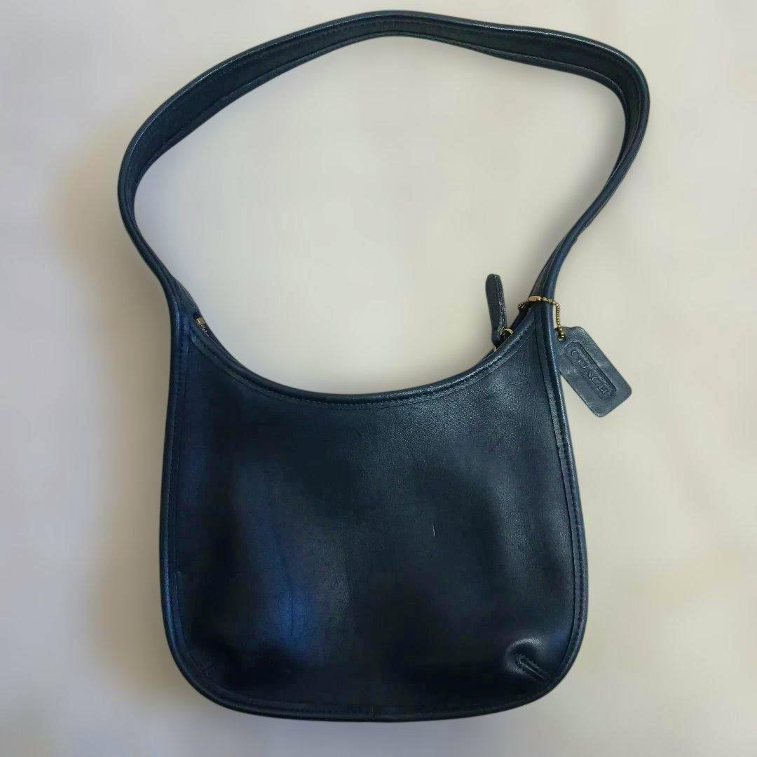 Black Coach leather shoulder bag with a single strap and attached hang tag shown flat on a neutral background.