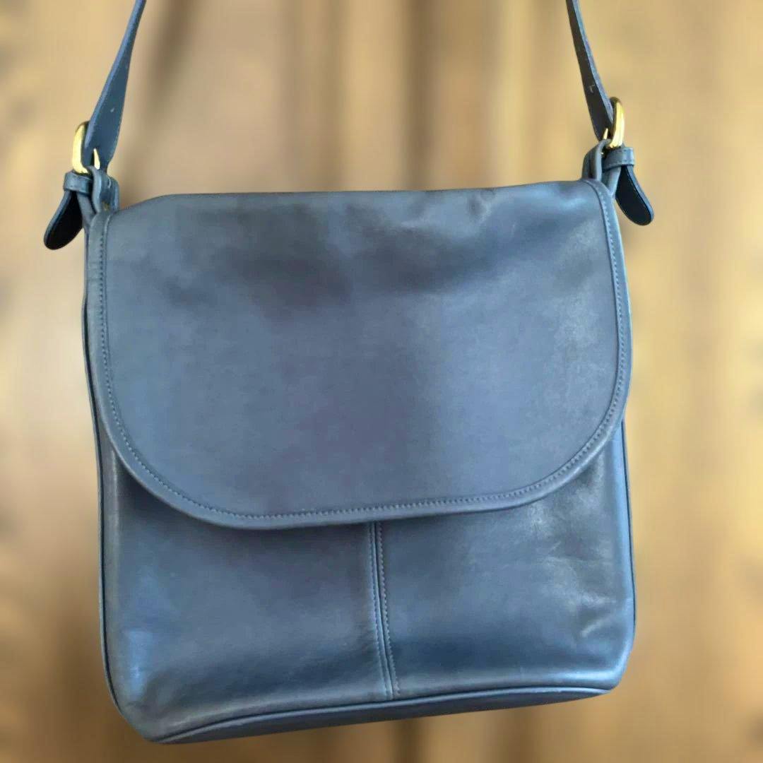 Front view of the blue-gray cow leather Coach shoulder bag with flap closed and single shoulder strap.