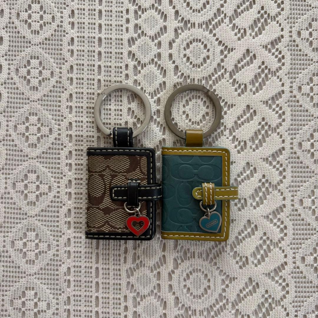 Two vintage Coach book-shaped bag photo charms with small heart pendants on a lace background.