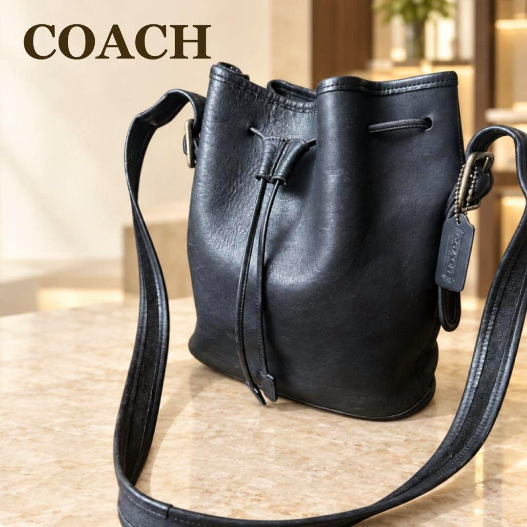 Black Coach leather drawstring shoulder bag shown on a marble surface with its shoulder strap visible.