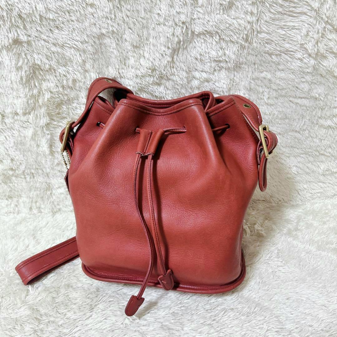 Red cow leather drawstring (bucket) shoulder bag (Coach) shown on a white textured background.