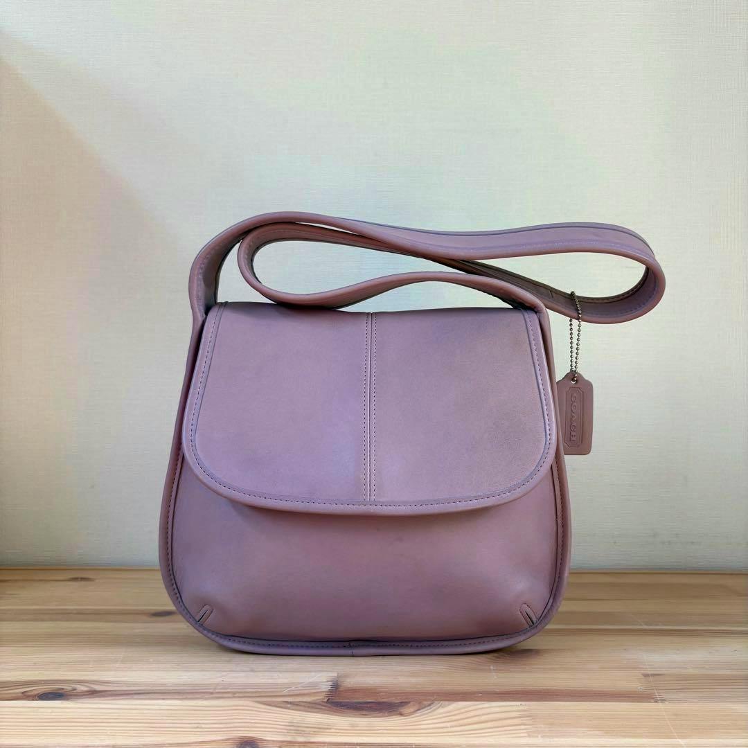 Front view of the vintage Coach Ergo bag in lavender purple leather with a flap closure and hanging Coach tag on a wooden surface.