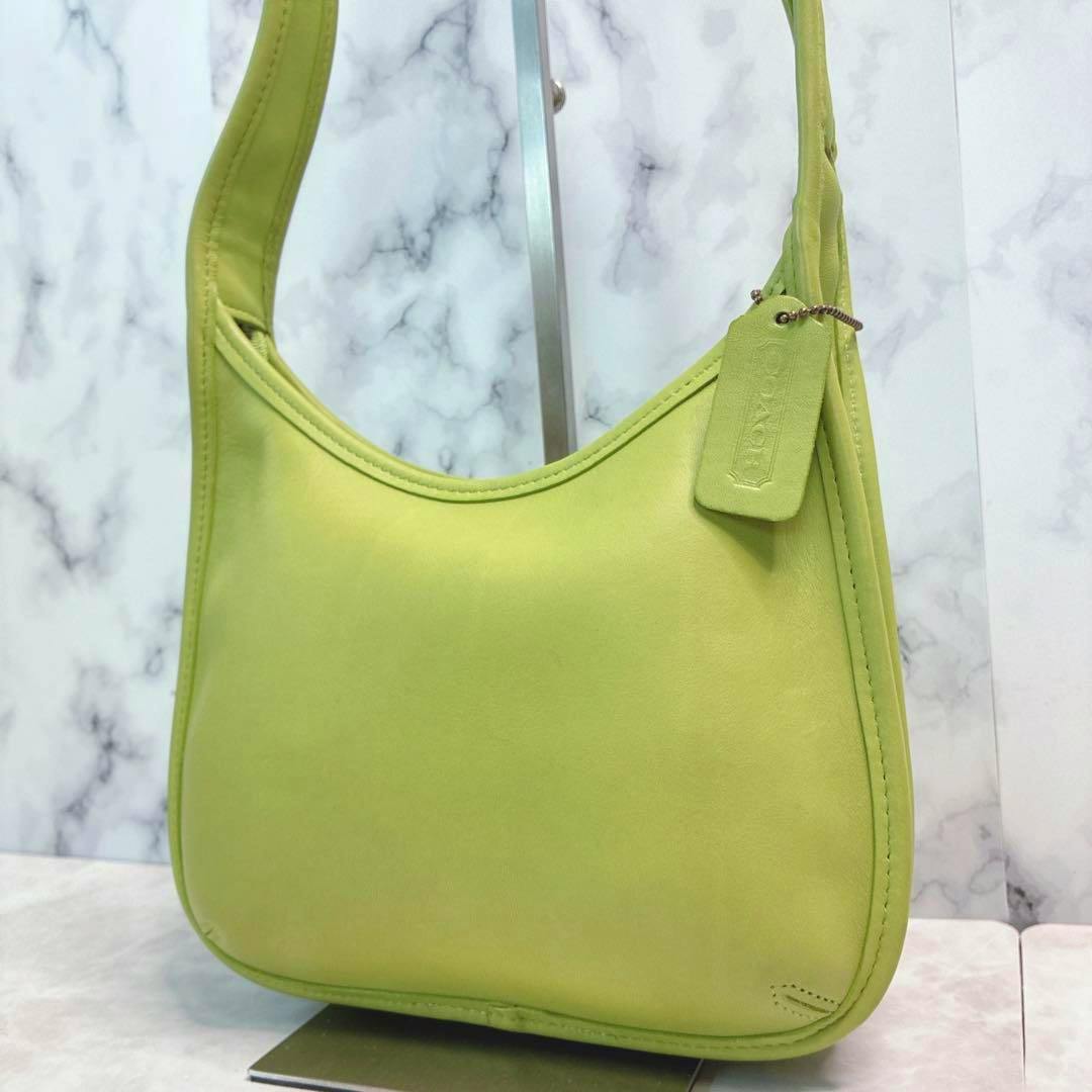 Green leather Coach hobo bag with a leather hang tag displayed on a stand.
