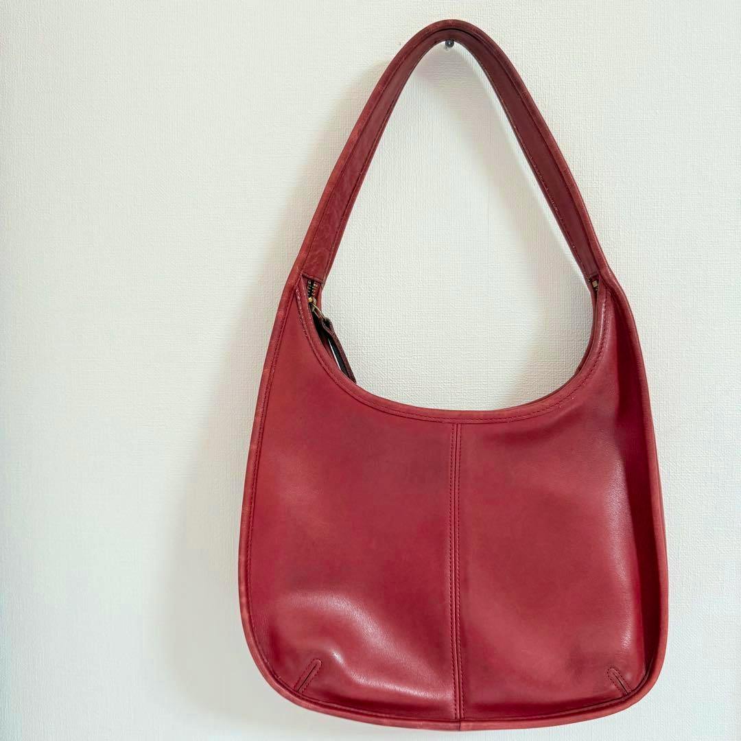 Red vintage Coach leather shoulder bag hanging against a light wall.