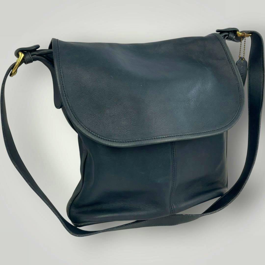 Front view of a navy Old Coach leather shoulder bag with a flap, adjustable strap, and hanging charm.