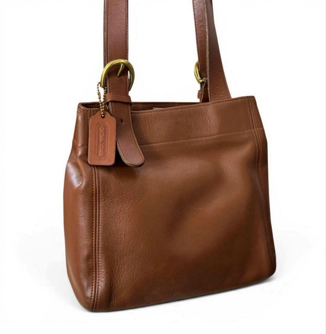 Brown glove-tanned leather shoulder tote bag front view showing leather hang tag, straps, and brass hardware.