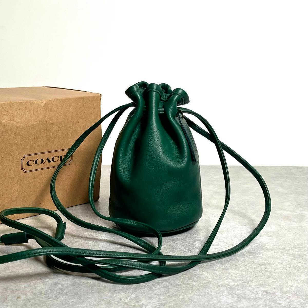 Vintage COACH green drawstring shoulder bag in glove-tanned leather displayed with its long straps beside a Coach box.