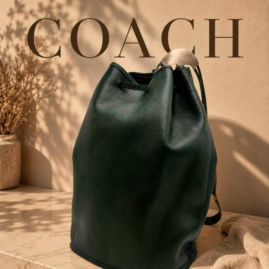 Green leather Coach vintage shoulder bag photographed upright on a stone surface with dried plants and a neutral backdrop.