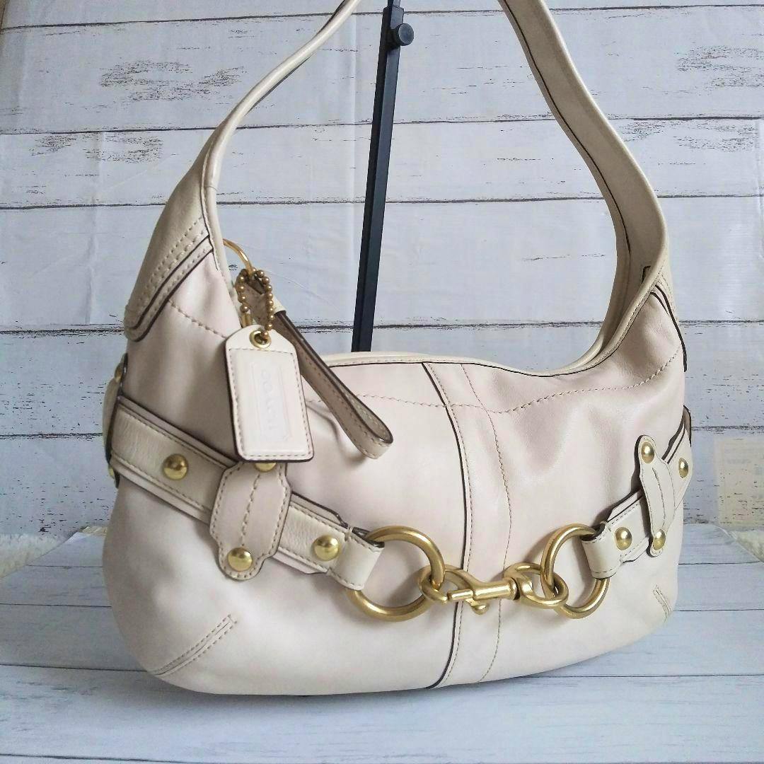 Vintage Coach hobo handbag in light cream cow leather with gold ring hardware displayed hanging on a stand.