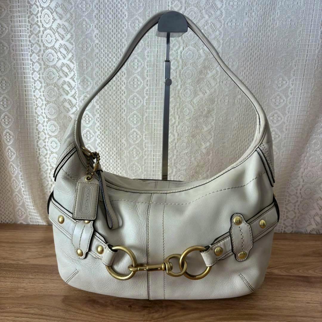 Vintage Coach hobo shoulder bag (cow leather) with prominent front gold-tone hardware and a hanging Coach leather tag displayed on a stand.