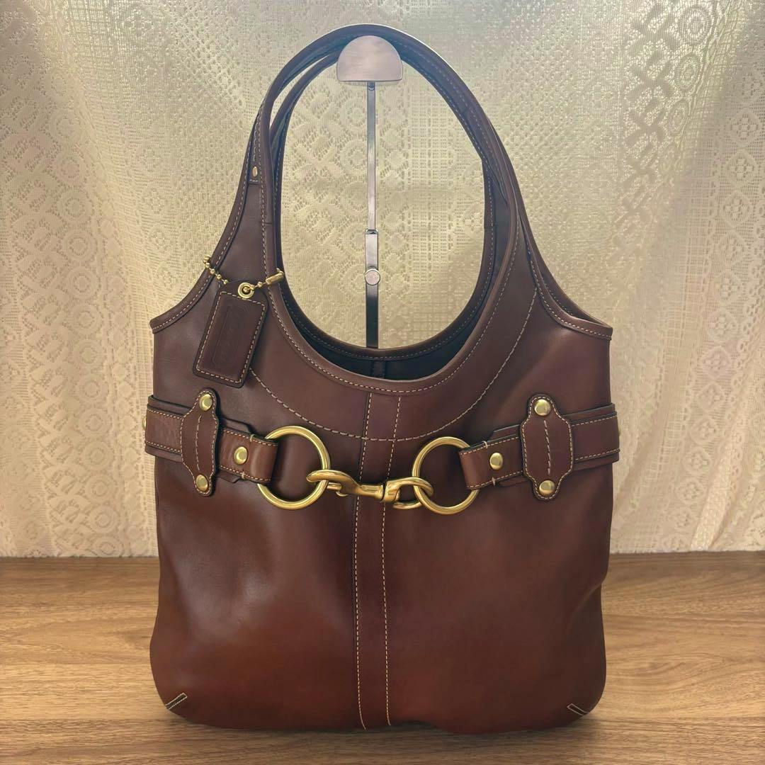 Brown vintage Coach hobo shoulder bag in cow leather with gold-tone horsebit hardware displayed on a stand.