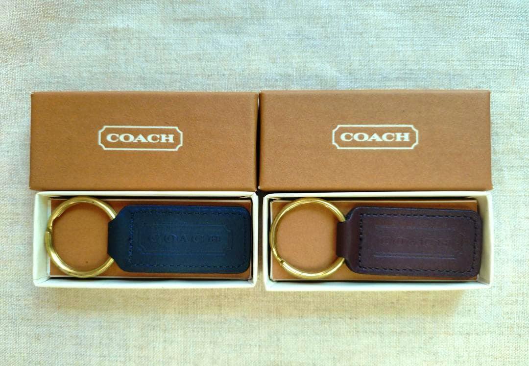 Two Coach keyrings, one black and one brown, each with a brass ring inside their boxes.