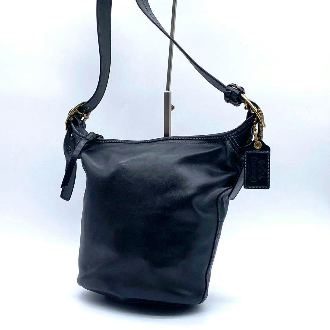 Black Coach leather bucket shoulder bag with shoulder strap and leather hang tag on a white background.