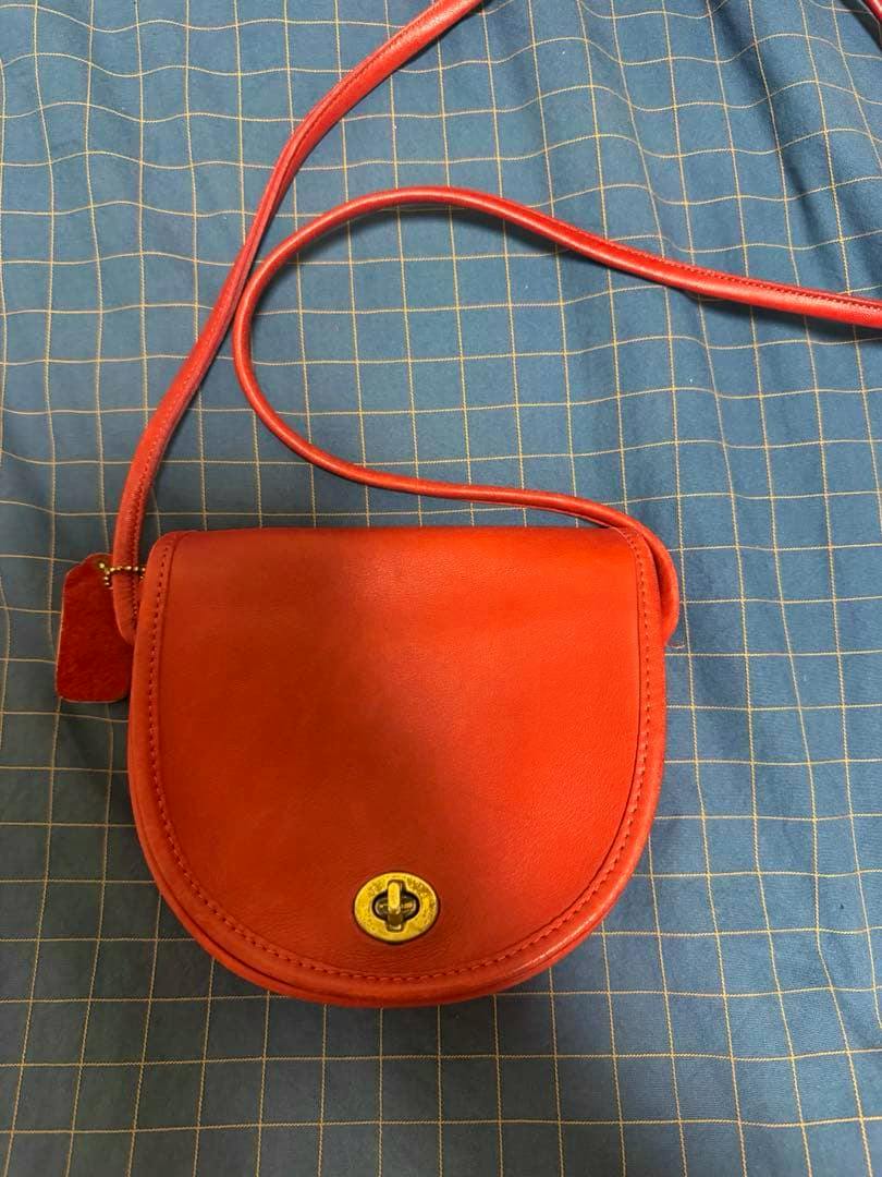 Red leather vintage COACH shoulder bag with a flap and gold turn-lock closure on a blue checkered background.