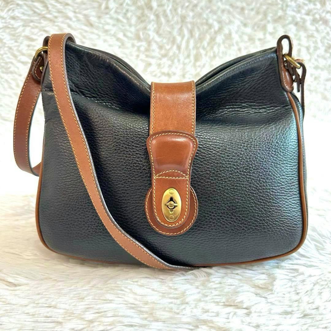Front view of a black pebbled leather shoulder bag with brown leather trim and a brass turn-lock closure.