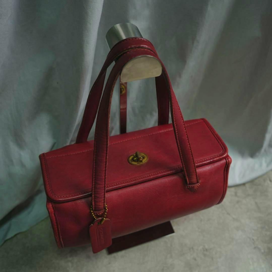 OLD COACH red leather square handbag with a dial lock and two top handles displayed on a metal stand.