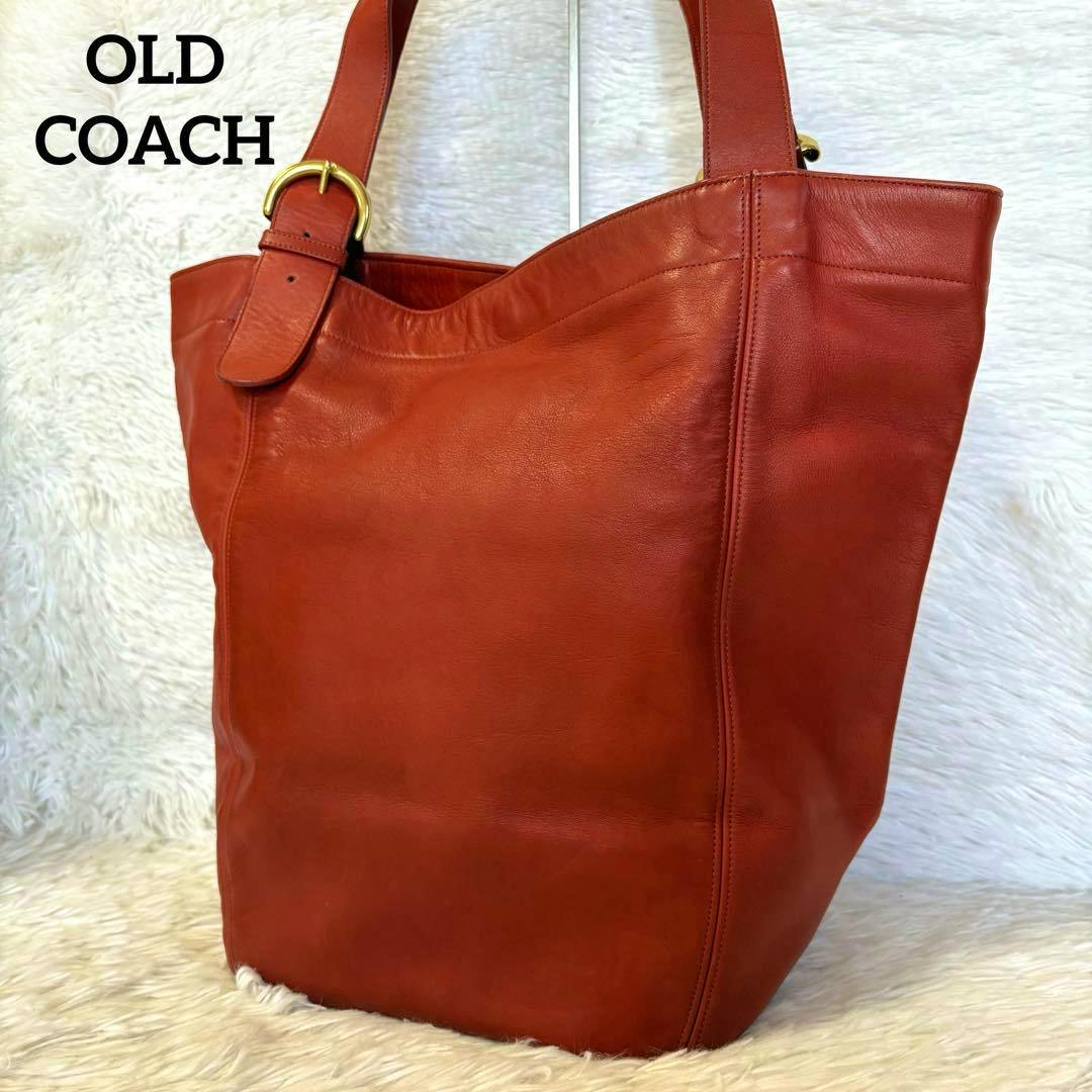 Red cow-leather Old Coach large tote bag with shoulder straps and a gold buckle shown against a white fur background.