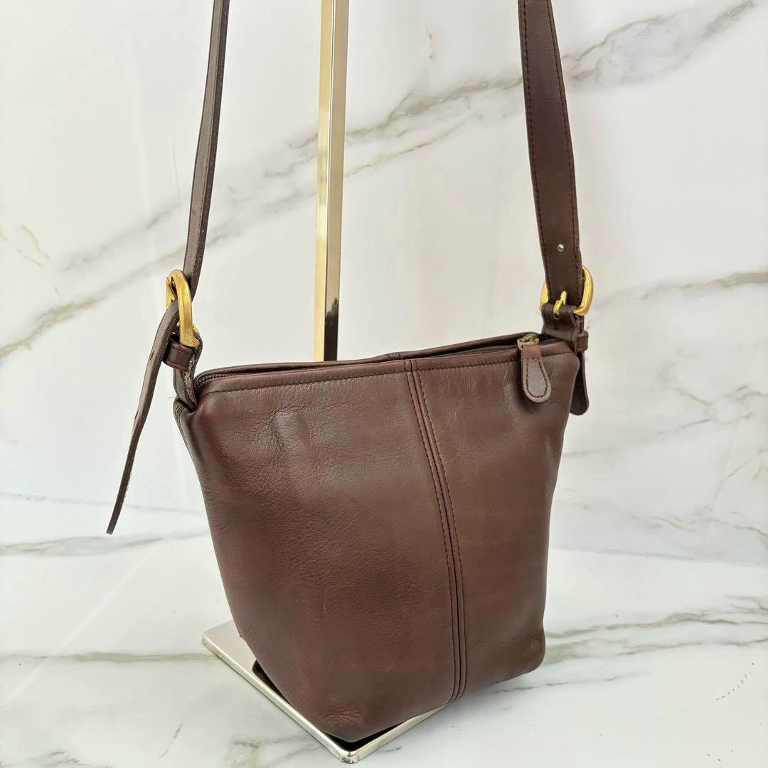 Brown leather Old Coach MacDougal zip shoulder bag hanging on a stand with strap, zipper, and front seam visible.