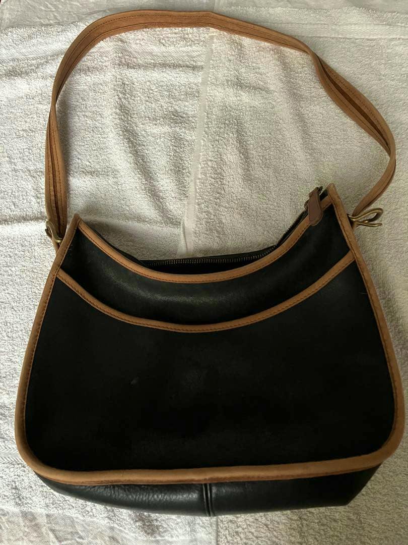 Top-down view of a black and tan leather shoulder bag laid flat on a light towel.