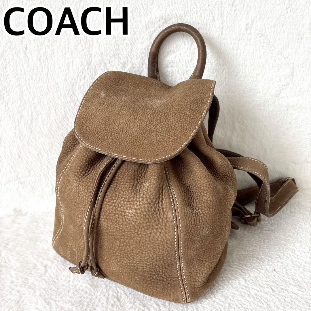 Vintage COACH nubuck drawstring backpack in brown shown at an angle on a white background, with flap, drawstring closure, and shoulder straps visible.