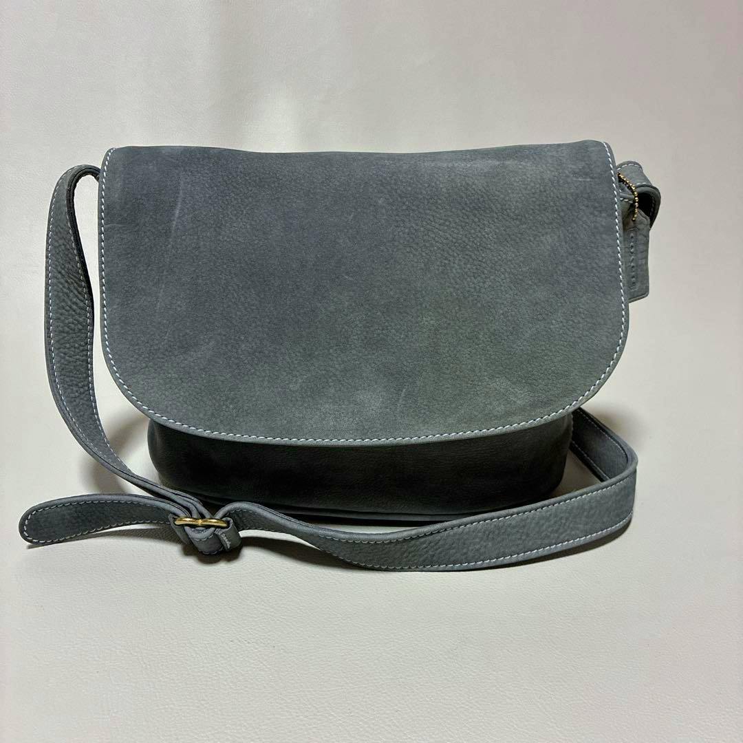 Gray nubuck cow leather Coach shoulder bag with flap closure and adjustable crossbody strap shown from the front.