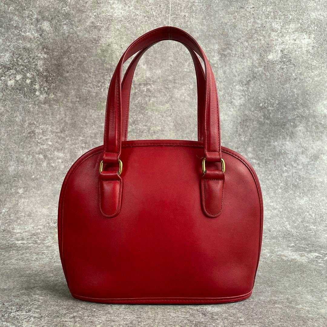 Front view of a red dome-shaped cow leather Coach handbag with double top handles and gold-tone hardware.