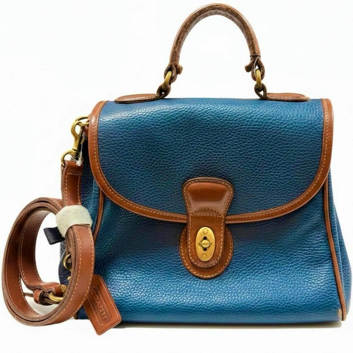 Front view of a vintage navy leather Coach Sheridan 2-way handbag with brown trim, top handle, turn-lock closure, and detachable shoulder strap.