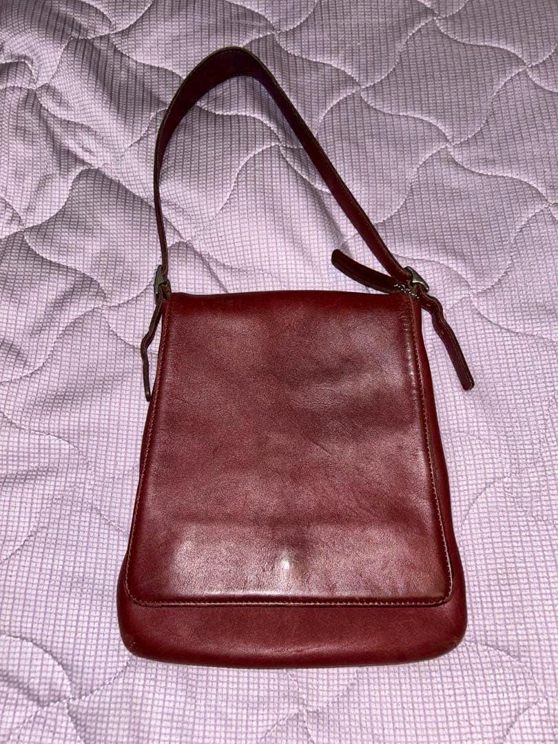 Bordeaux cow leather COACH shoulder bag laid flat showing the front flap and single shoulder strap.