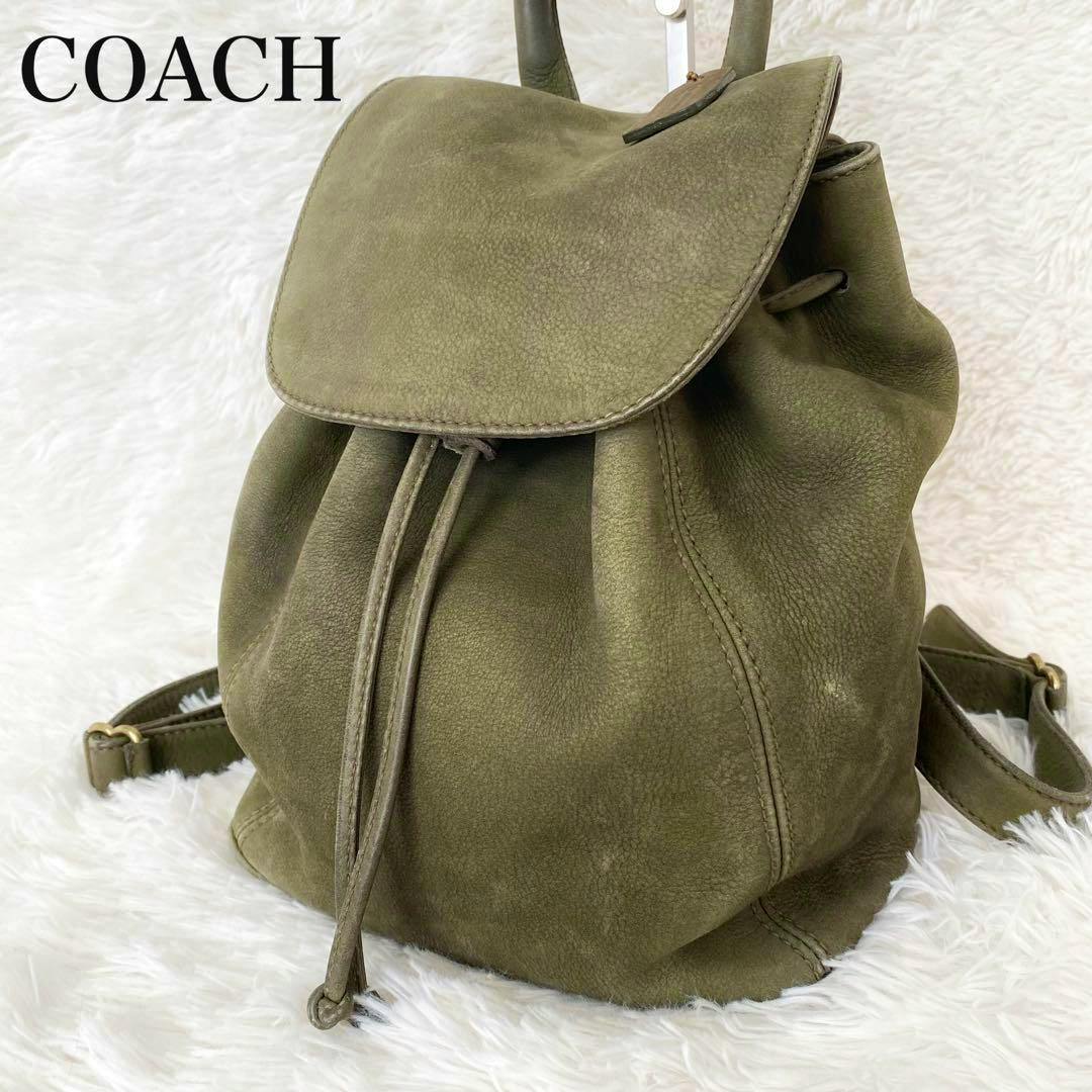 Vintage Coach small khaki leather backpack with flap and drawstring closure displayed on a white fur background.