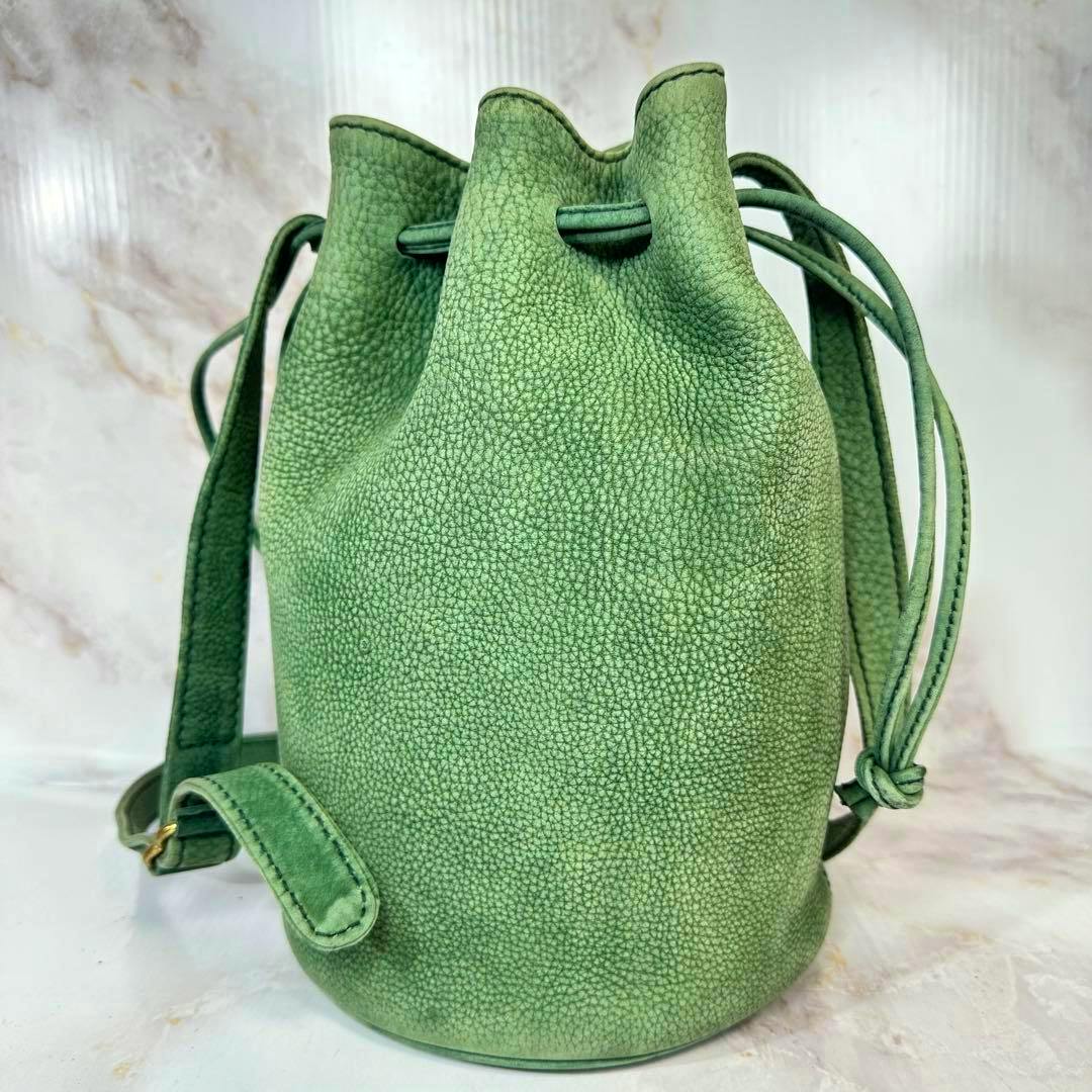 Green nubuck drawstring bucket bag with a shoulder strap standing on a light background.