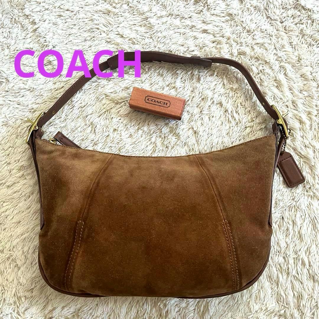 Brown suede Coach shoulder bag with leather strap and Coach hangtag lying on a light shag rug.