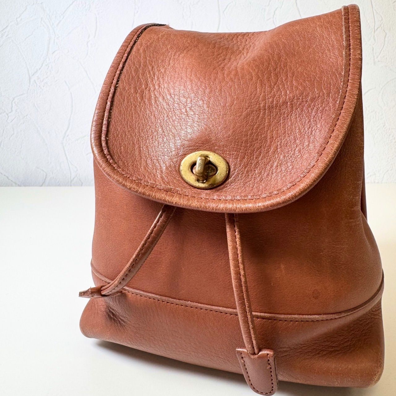 Brown glove-tanned leather COACH rucksack backpack with turn-lock flap displayed on a white surface.