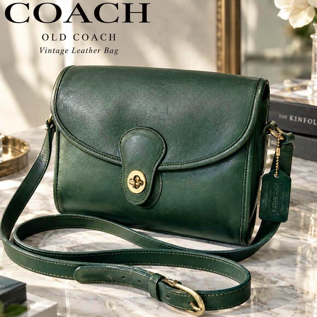 Green Coach turn-lock leather shoulder bag with long strap and hang tag displayed on a marble surface.