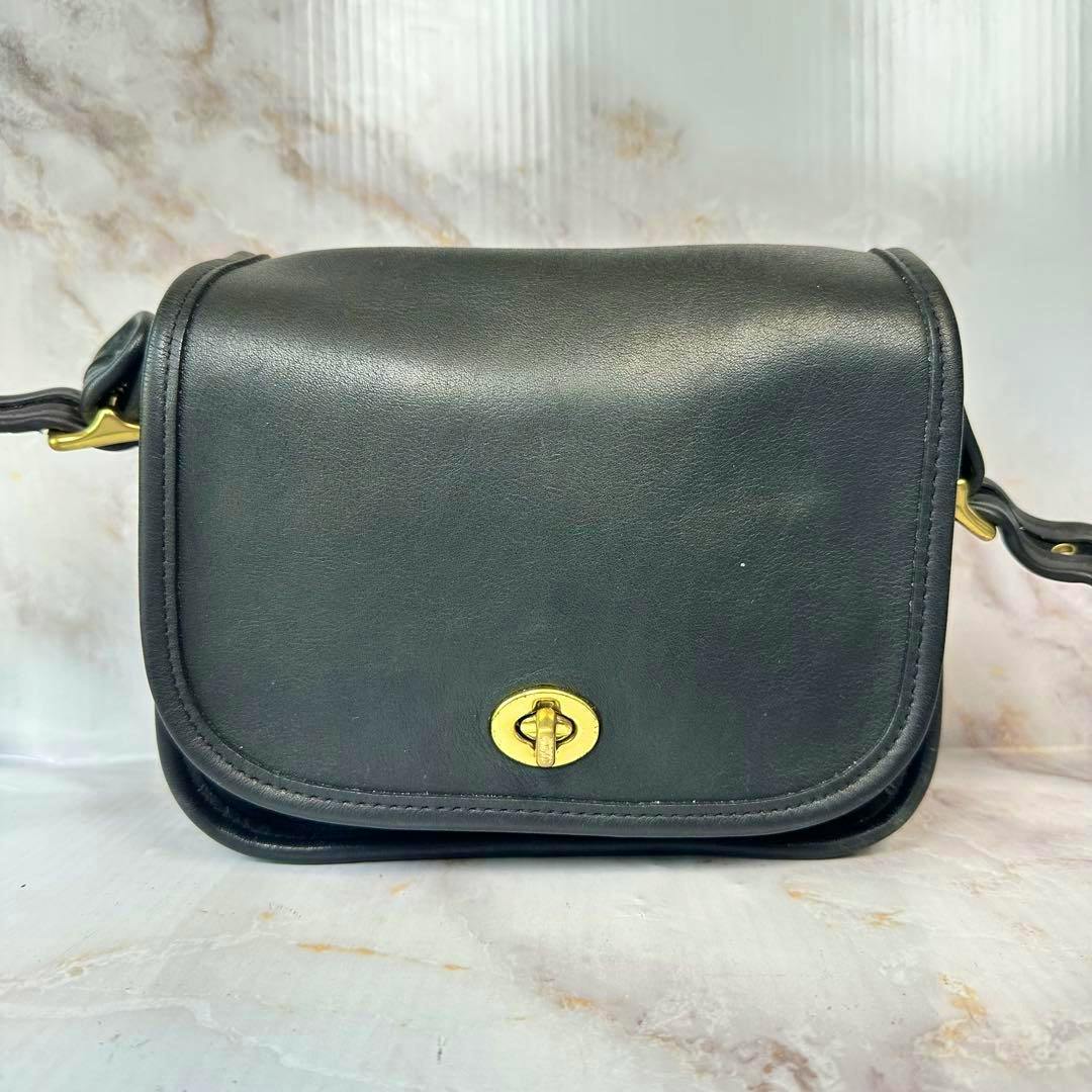 Front view of a black Coach cow leather shoulder bag with a gold turnlock closure and attached strap.
