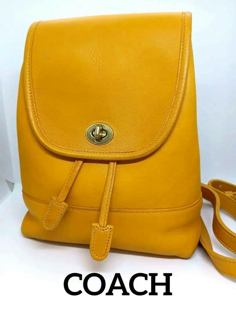 Yellow leather Coach backpack shown from the front with a turn-lock flap and drawstring straps.