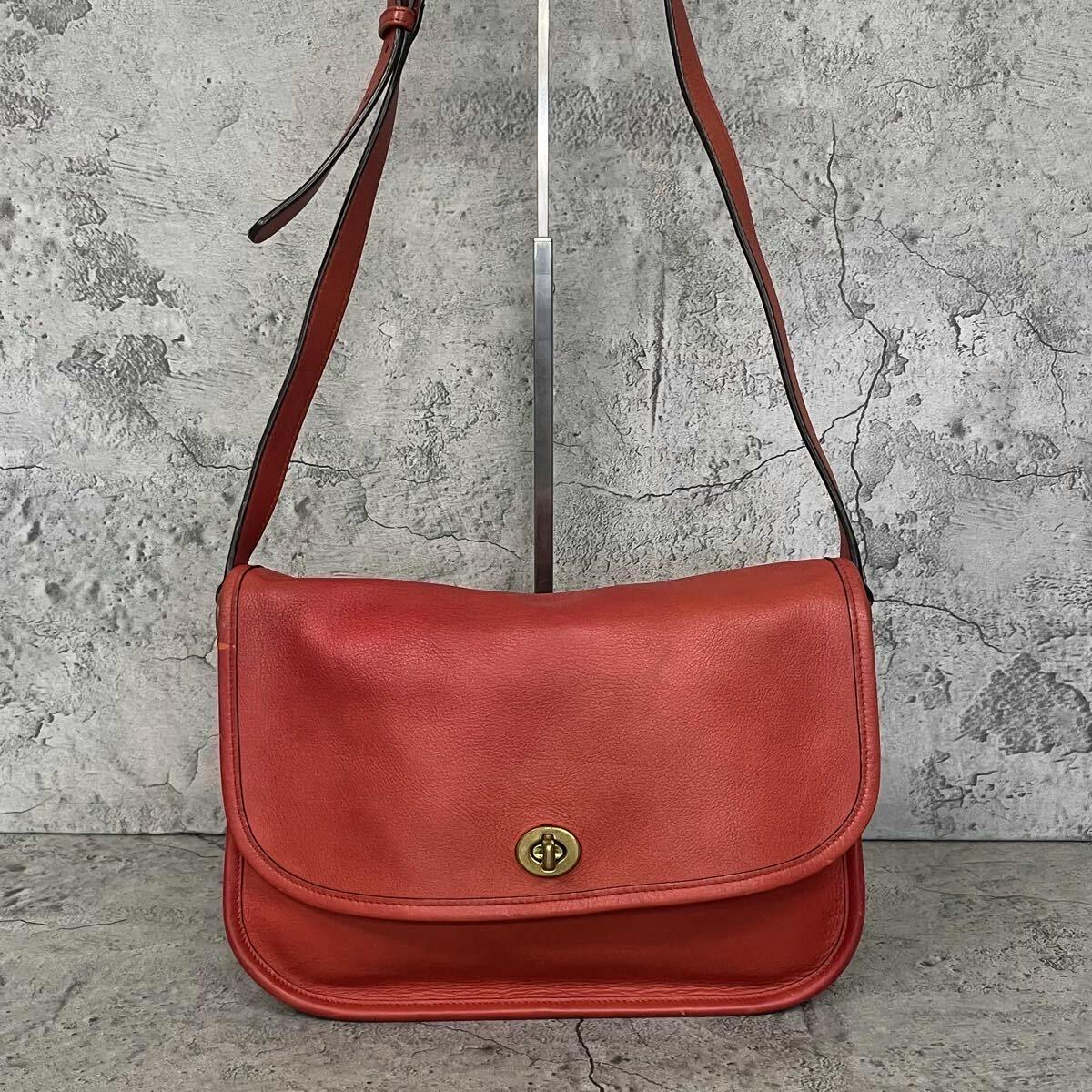 Front view of a vintage red Coach leather shoulder bag with a gold turnlock and adjustable shoulder strap.
