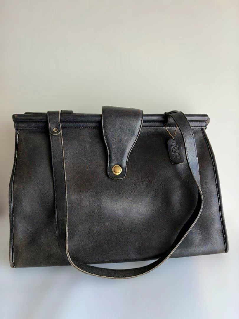 Black Old Coach leather tote bag with a turn-lock flap and single shoulder strap photographed against a plain background.