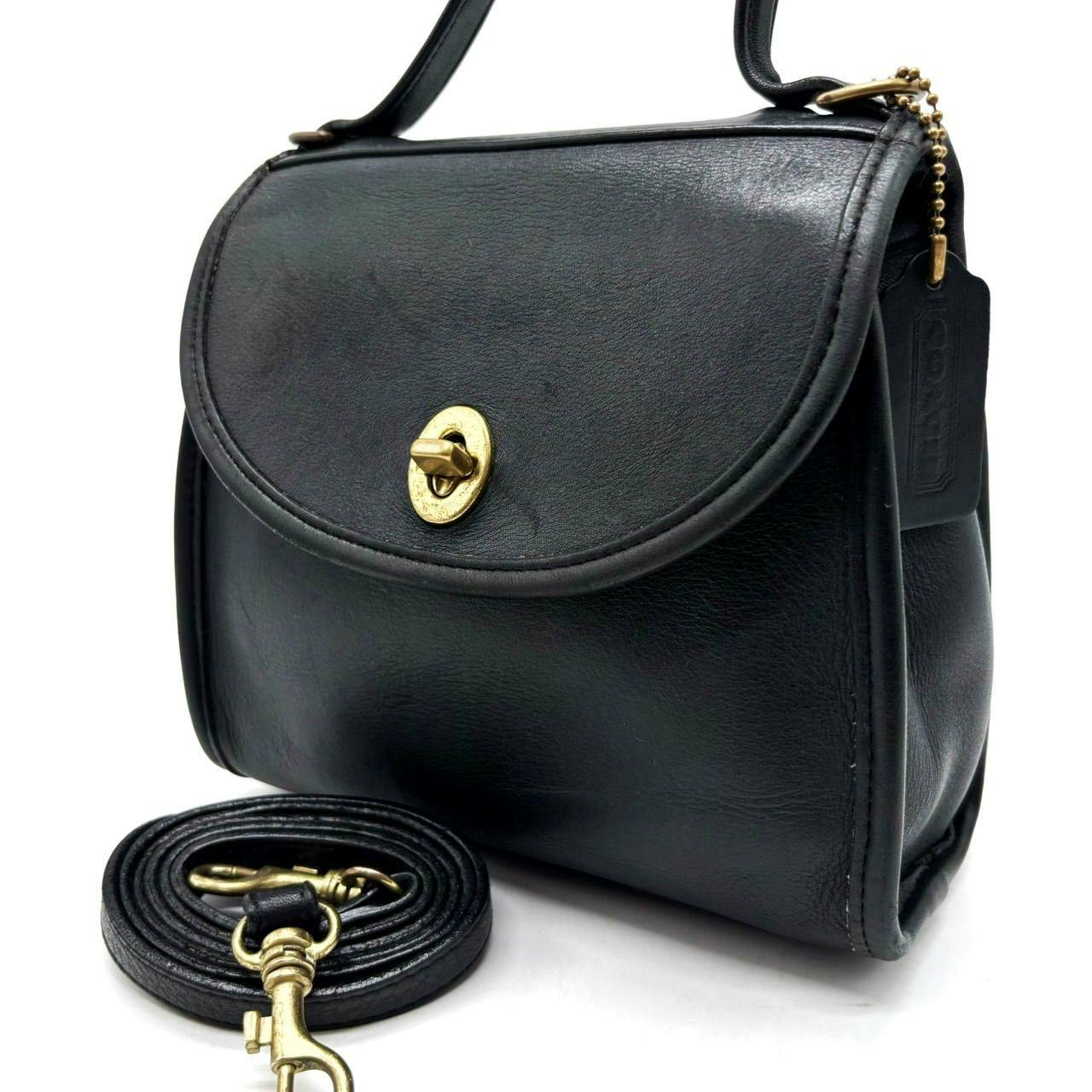 Black leather Coach turn-lock 2way shoulder bag shown from front-right with coiled detachable strap and gold hardware.